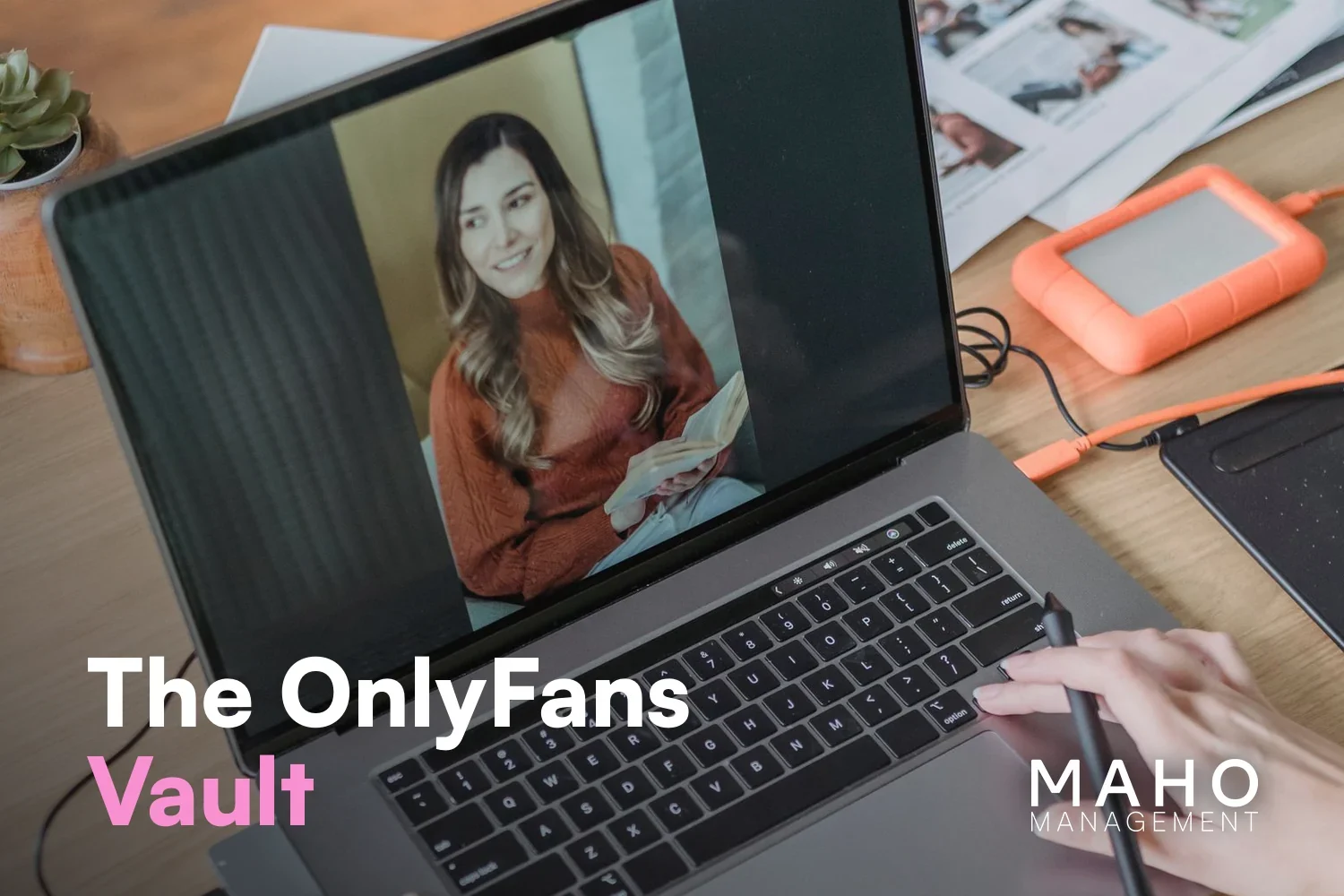Laptop showing a portrait photo, next to a pen tablet, an external hard drive and printed photos (sorting content for the OnlyFans vault)